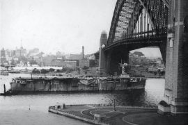 The Royal Navy aircraft carrier HMS Vindex passing under the Sydney Harbour Bridge with 300 ex-prisoners of war returning home. (Source: City of Sydney Archives)