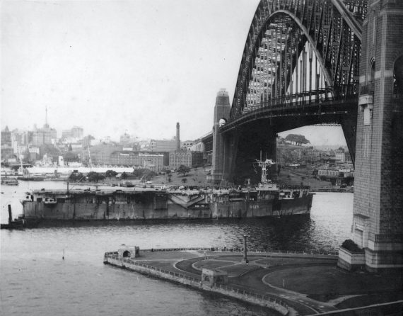 The Royal Navy aircraft carrier HMS Vindex passing under the Sydney Harbour Bridge with 300 ex-prisoners of war returning home. (Source: City of Sydney Archives)
