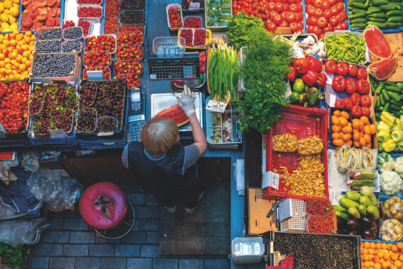 Gourmet Trails Europe. Top view of a woman behind a counter at a fruit and vegetable kiosk in the Balti Jaama Turg market.