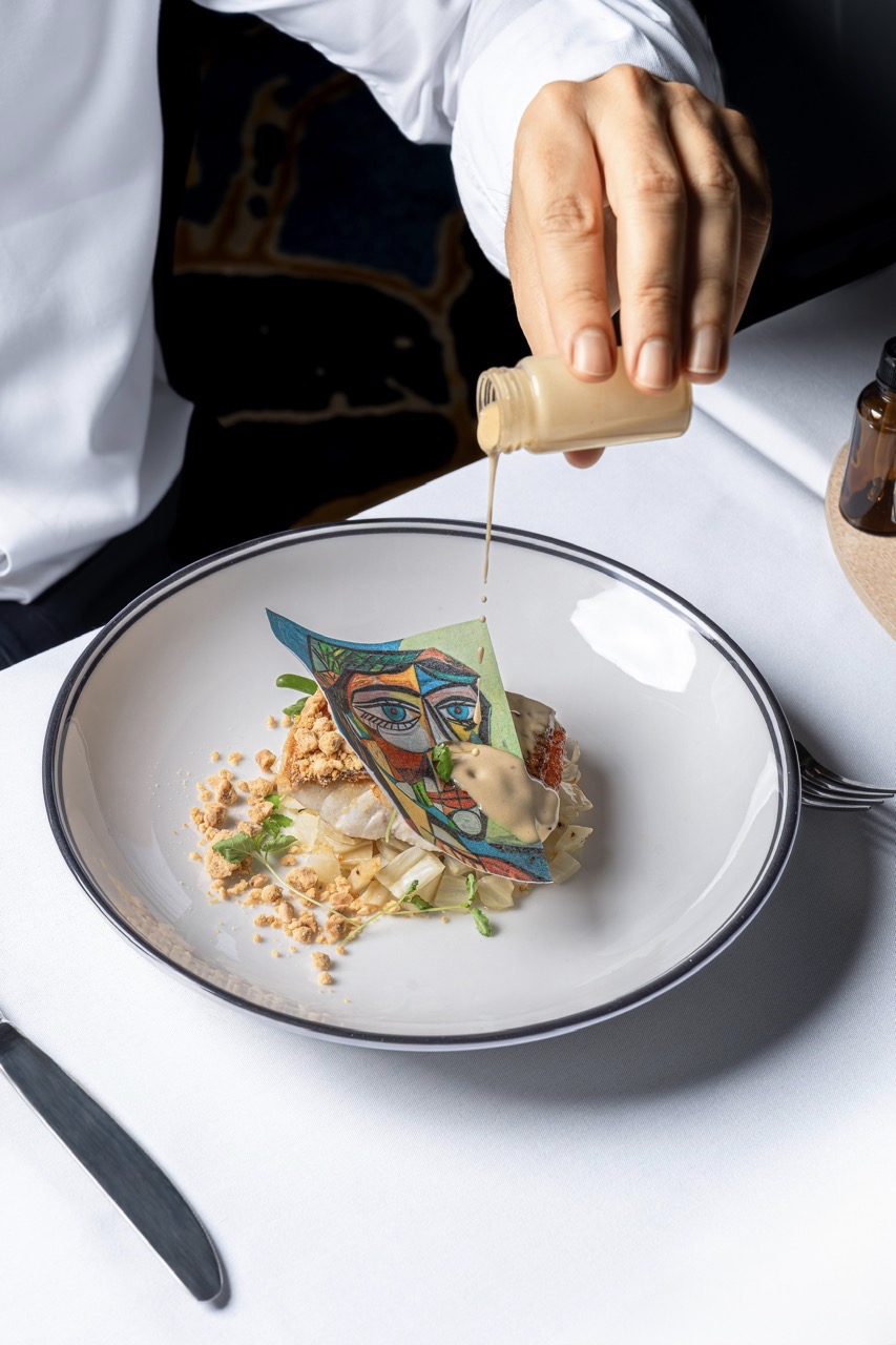 Black garlic beurre blanc is poured over the fish in the Picasso course.